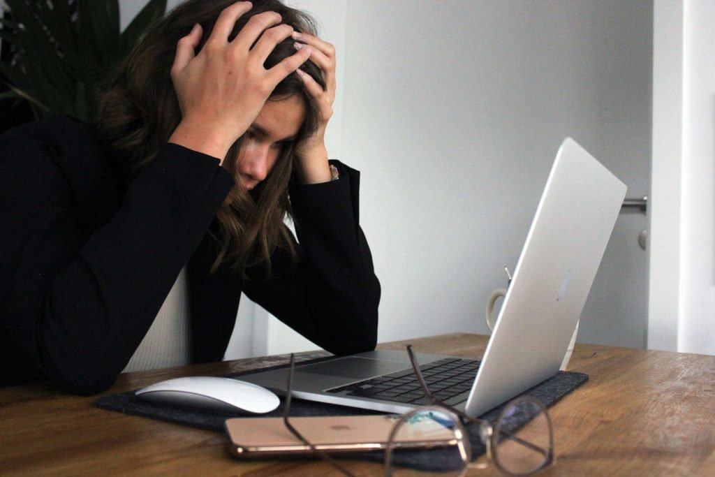 woman with her head in her hands staring at her computer screen. Perhaps she is hungry but overwhelmed at the thought of tracking her intake and symptoms